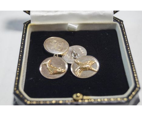 A pair of silver cufflinks, one oval panel with a pheasant in flight, the other with a leaping salmon, all against an engine 