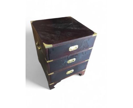 An ebonised and brass-bound chest of three short drawers, with brass swing handles within sheltered frames. Upon ogee-bracket