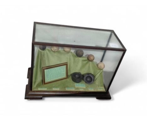 A display of golf balls in a glass case, together with a gold ball mould