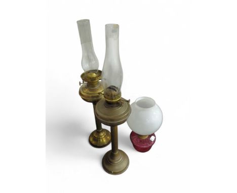 An oil lamp with tall brass column, another similar and another with cranberry glass reservoir (3)