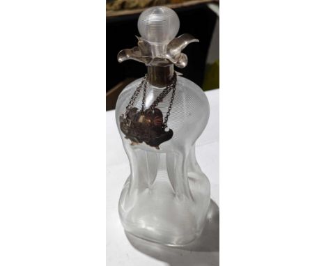 A glass decanter with silver collar and three labels. The glass artfully inhaled at the centre, with a stripy complexion thro