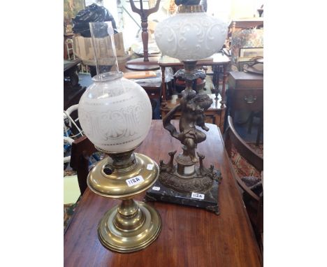 AN OIL LAMP with a white glass font supported by a spelter cherub and a similar brass oil lamp (2)
