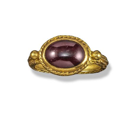 A garnet and gold ring in the late Roman Empire style, the oval cabochon garnet is set in a twisted rope mount between two sh