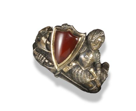 A 19th century silver-gilt Medieval Revivalist ring, c1890, designed as a recumbent Crusader in armour with carnelian shield 