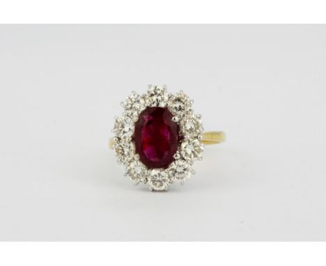 A yellow and white metal (tested 18ct gold) cluster ring set with an oval cut ruby surrounded by brilliant cut diamonds, appr