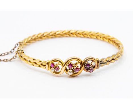 A late Victorian ruby and diamond 15ct gold bangle, comprising three open scrolled details to the front each set with two rou