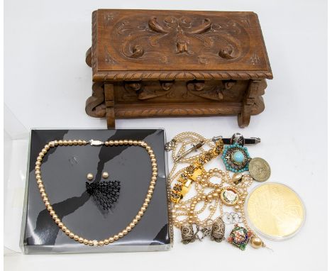 A carved wooden box containing costume jewellery including faux pearl necklaces, gilt metal bracelets, enamel brooch and vari