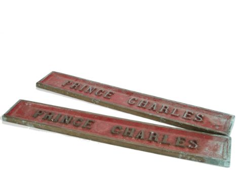 A pair of cast brass plates 'Prince Charles' with raised brass letters against a red-painted background, measuring 19" x 3" a