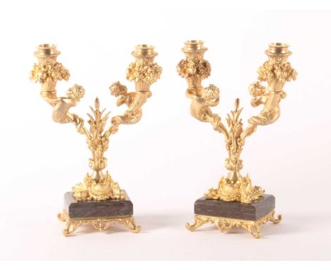 A pair of gilt bronze twin branch table candelabra, each decorated with putti and mounted upon a polished hardstone plinth, h