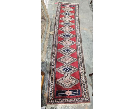 Eastern red ground runner with one row of 12 lozenges of alternating colurs, multiple geometric borders, 300cm x 74cm&nbsp;