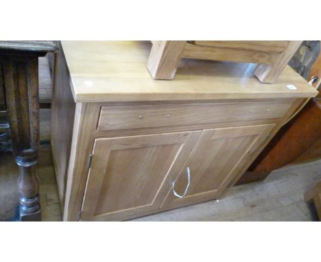 A contemporary light oak side cabinet with a single frieze drawer above two panelled doors, lacking handles.