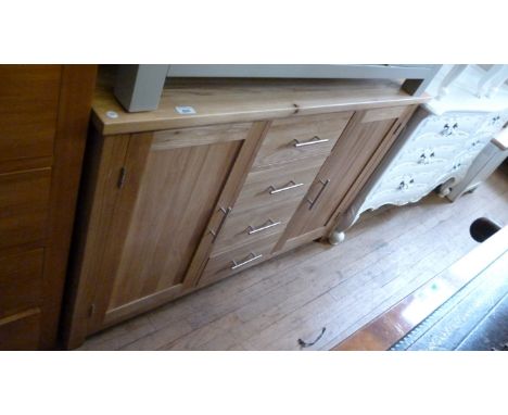 A contemporary light oak sideboard, the rectangular top above four central drawers and flanked by two cupboard doors, each wi
