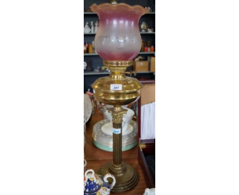 A 20th Century brass oil lamp raised on Corinthian column supports, with frosted pink and clear glass shade.