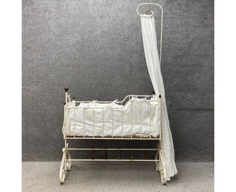 A Victorian white painted cast iron cot with a swinging action having a tall scrolled stem with a draped curtain with brass f