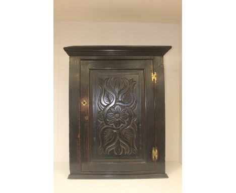 A 19th Century ebonised oak wall hanging corner cupboard, the single panel door with stylised foliage carved decoration, open