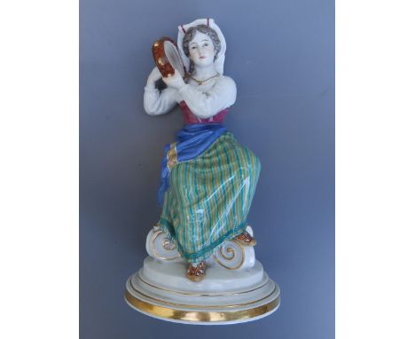 A Meissen porcelain figure of a female tambourine player in folk costume, seated on an upturned Corinthian capital, 7.75" hig