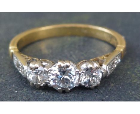 A three stone  claw set diamond ring, small diamonds to shoulders, on 18ct. shank.  Finger size K.