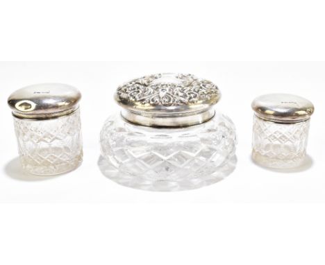 Three cut glass dressing table jars with hallmarked silver covers including an example with repoussé detail of birds and scro