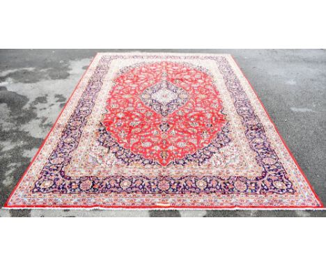 A Persian Kashan hand woven wool carpet, decorated with a central medallion against a red ground with all over floral detaili