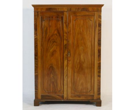 Edwardian mahogany wardrobe in the Georgian style, having a dentil cornice over two recessed moulded panel doors opening to h