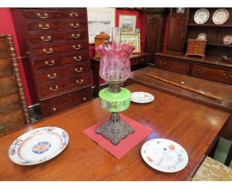 A late Victorian oil lamp, the cranberry etched shade over a green painted glass reservoir to a pierced cast metal base
