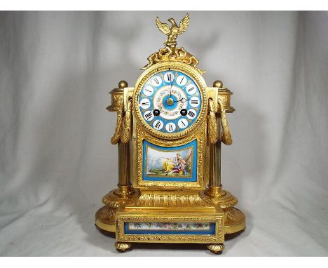 A late 19th/ early 20th century mantel clock, the classically styled gilded case with insert porcelain panels having painted 