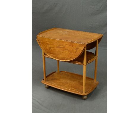 A BLONDE ERCOL ELM DROP-LEAF THREE TIER TEA TROLLEY, the rounded drop leaves to form an oval, galleried top on orbit castors,