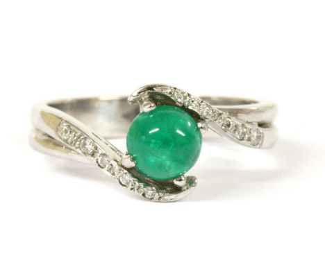 An 18ct white gold emerald and diamond crossover ring, a round cabochon emerald with a stated weight of 0.97ct, four claw set