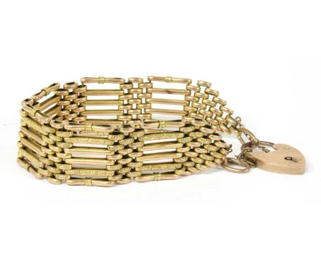 A gold six row gate bracelet, with plain polished and textured links, with gathered outer bars, to heart shaped padlock clasp