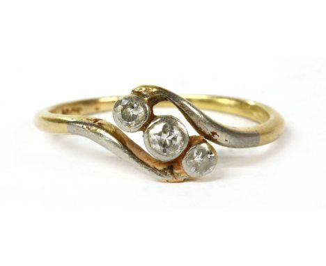 A gold three stone diamond ring, graduated brilliant cut diamonds, rub set, to crossover shoulders and a plain polished shank