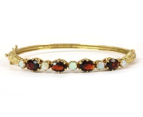 A 9ct gold opal and garnet hinged bangle, c.1980, an alternating row of round cabochon opals and oval mixed cut garnets, claw