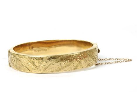 A 9ct gold hollow oval hinged bangle, with hand engraved decoration to both halves, to concealed box clasp and safety chain, 