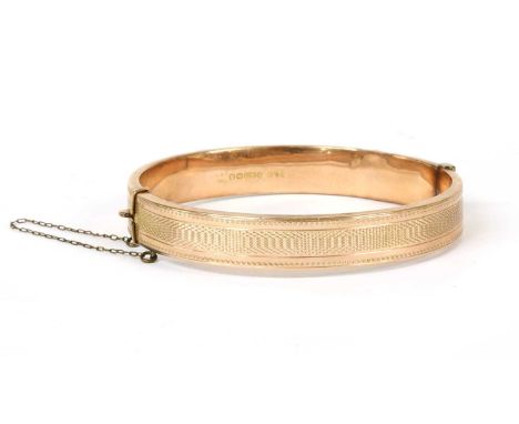 A 9ct gold oval hollow hinged bangle, with engine turned decoration, concealed box clasp and metal safety chain, Birmingham 1