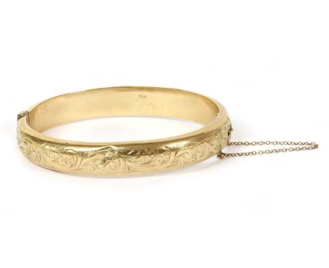 A 9ct gold oval hollow hinged bangle, with hand engraving to the upper half, concealed box clasp and safety chain, Chester 19