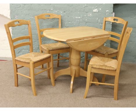 A light oak dropleaf dining table and set of four ladder back rush seat chairs.