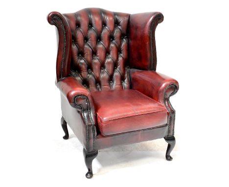 A modern button back wing armchair upholstered in oxblood studded leather, on cabriole legs.