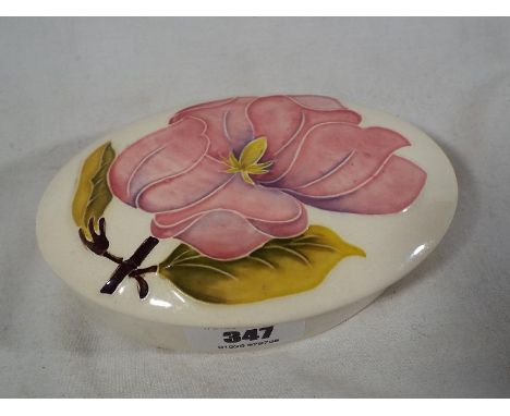 A Moorcroft Pottery lidded oval trinket box decorated with pink magnolia on an ivorine ground, 3.5 cm (h) x 13 cm (w) - Est £