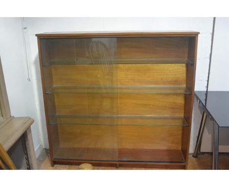 A 1970s teak upright open bookcase fitted three glass shelves with twin sliding glass panel doors, on plinth base (h. 133cm x
