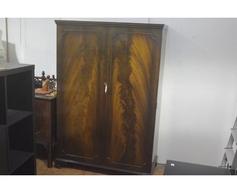 A 1920s/30s flame mahogany two door wardrobe, the moulded cornice above a pair of panel doors enclosing a plain interior, rai