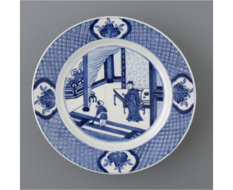 A CHINESE BLUE AND WHITE PLATE, KANGXI,  PAINTED WITH AN INTERIOR SCENE IN PANELLED DIAPER BORDER, THE UNDERSIDE WITH RUDIMEN