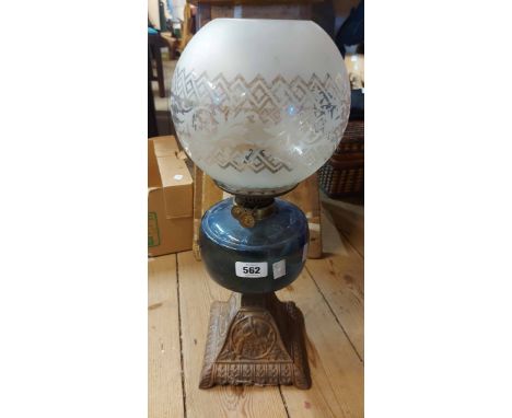 An antique oil lamp with bird decorated metal base and blue clear glass reservoir and decorative shade