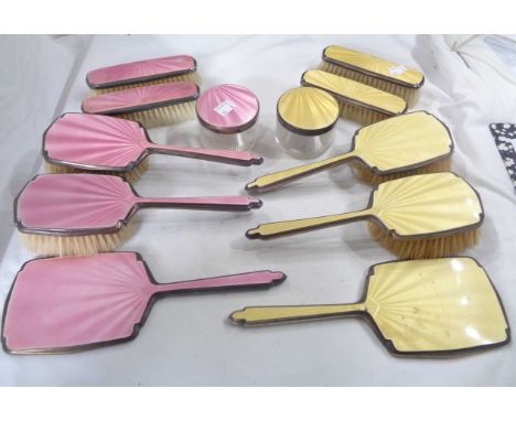 Two Art Deco six piece enamelled silver mounted dressing table brush, hand mirror and pot sets, one in pink, the other canary