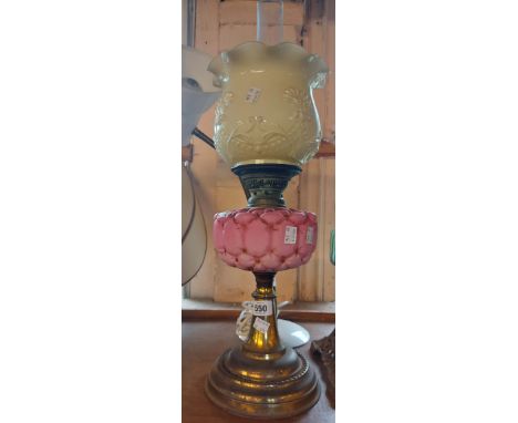 A brass based oil lamp with pink button back style glass reservoir and opaque glass shade