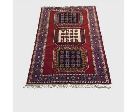 A wool Eastern carpet on red ground with triple medallion central panel, 172 cm x 120 cm.