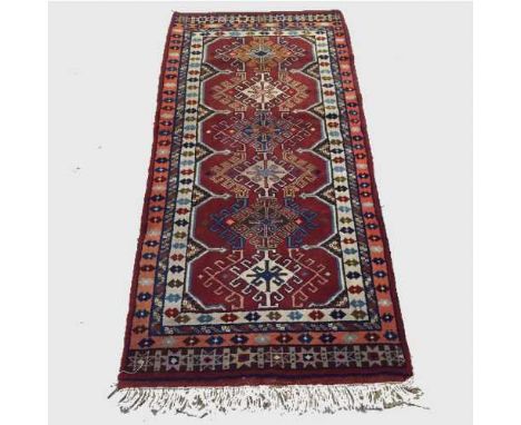 A wool Eastern carpet runner on red ground, 188 cm x 87 cm.