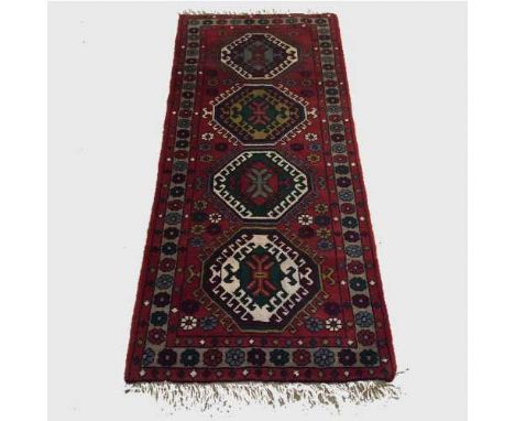A wool Eastern carpet runner on red geometric ground, 186 cm x 84 cm.