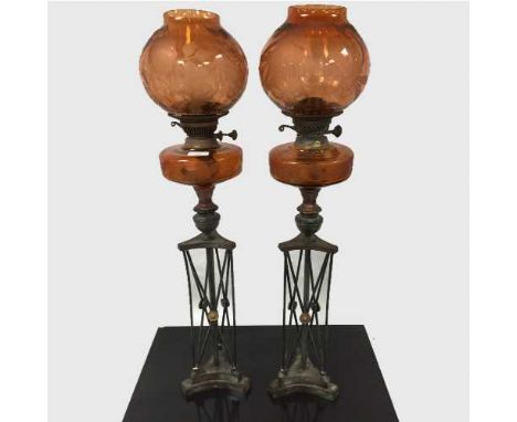 An unusual pair of Arts and Crafts bronze and orange etched glass oil lamps, on stepped plinth bases with slender bronze supp