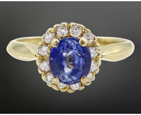 A sapphire and diamond cluster ring, the oval-cut sapphire within a border of twelve brilliant cut diamonds, within a claw mo