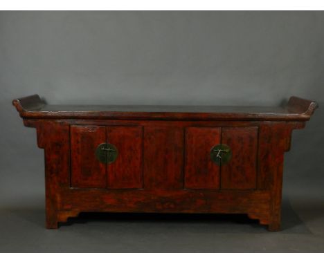 An early 20th century Chinese red lacquered altar cabinet, with a scroll moulded top above two cupboard doors enclosing drawe