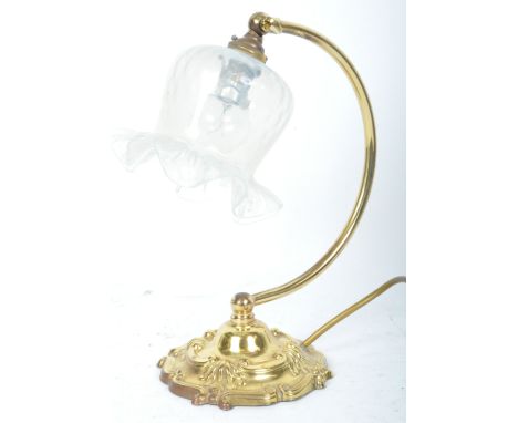 A vintage 20th century brass table lamp having a glass tulip shade over arched arm on a rococo manner base with moulded rocai